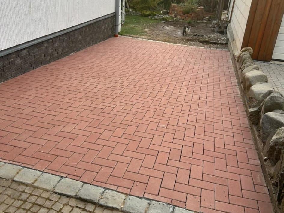 Neu verlegte Einfahrt aus rotem Rechteckpflaster, eingefasst von grauem Kleinpflaster